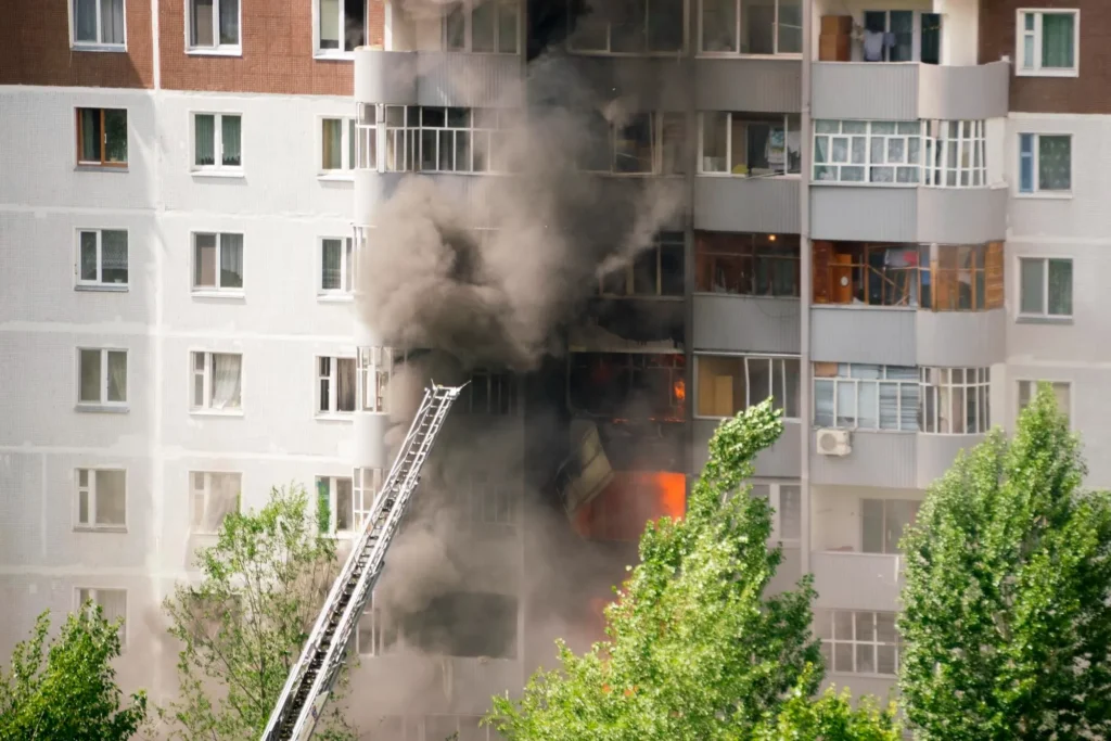 High-rise apartment fire with thick black smoke and flames, fire ladder extended.