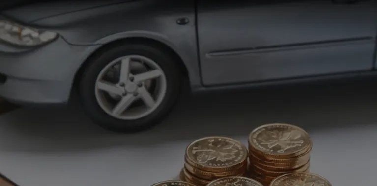 Close-up of stacked Canadian coins in front of a gray car tire and door.