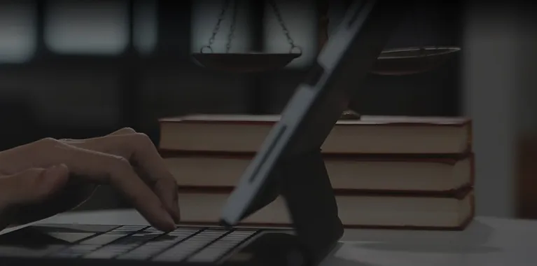 Person typing on a laptop keyboard with stacked books and scales of justice in the background.
