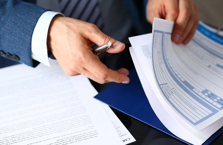 Close-up of a person in a suit holding a pen and reviewing printed documents.