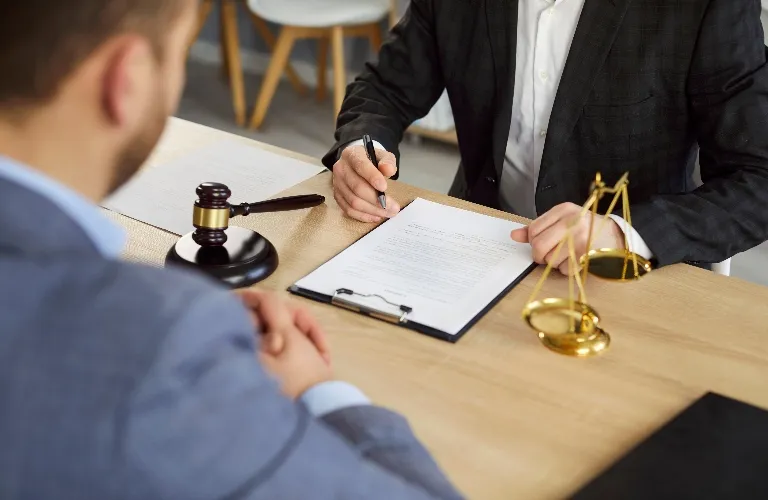 Two men in formal attire at a desk with legal documents, gavel, and scales of justice.