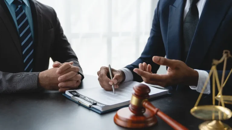 Two men in suits discussing legal documents at a desk with gavel and scales.
