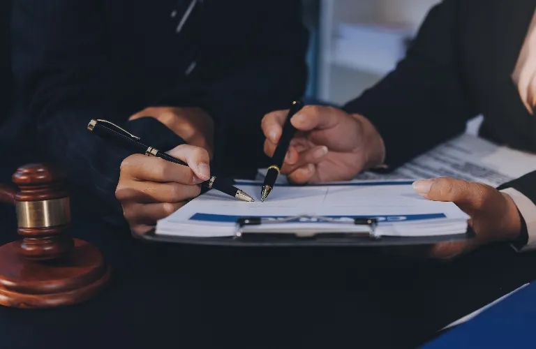 Two professionals reviewing a document on a clipboard with pens, next to a wooden gavel.