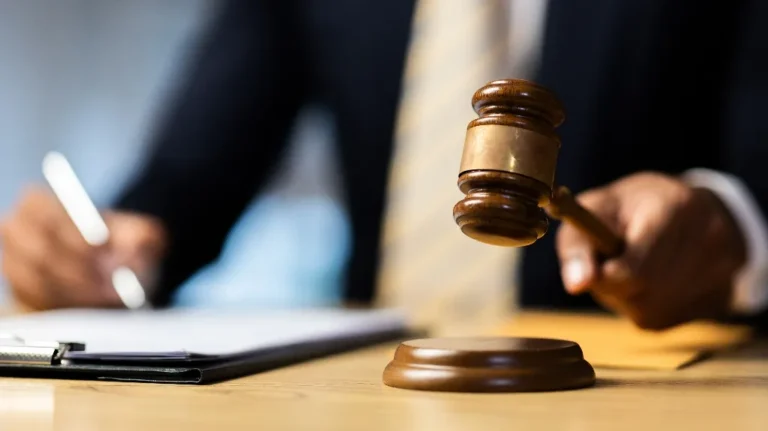 Close-up of a judge's hand holding a wooden gavel above a sound block on a desk.