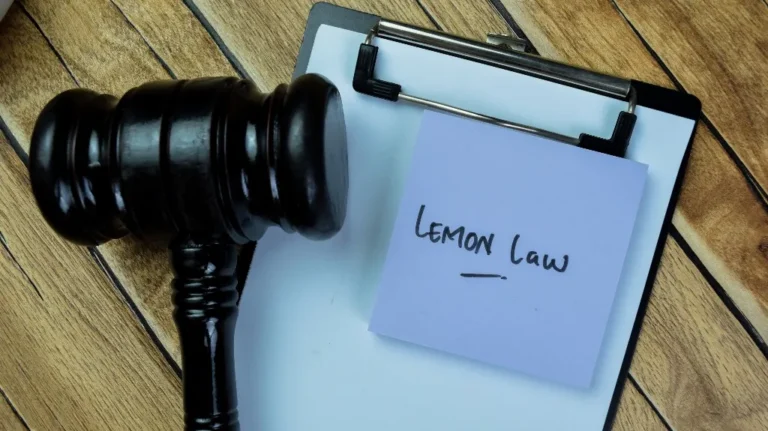 Wooden judge's gavel next to a clipboard with a note labeled "LEMON LAW" on a wooden surface.