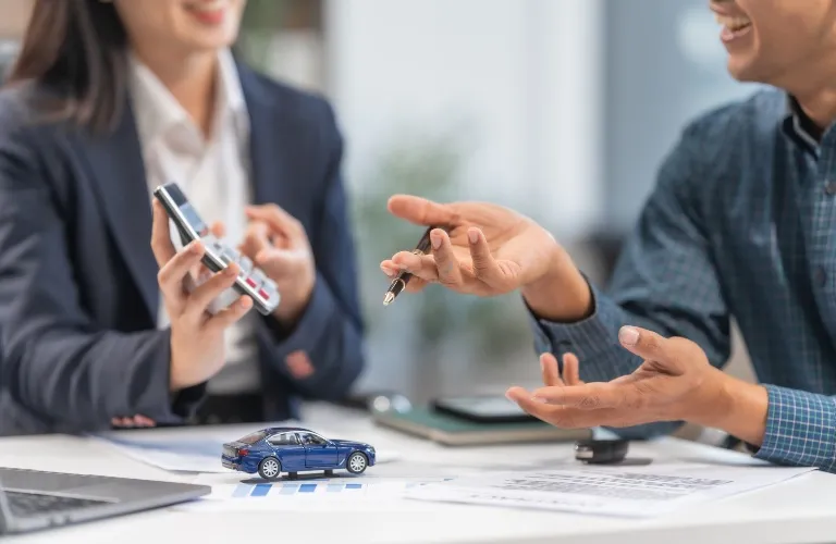 Two professionals discussing over car model and documents in office setting.