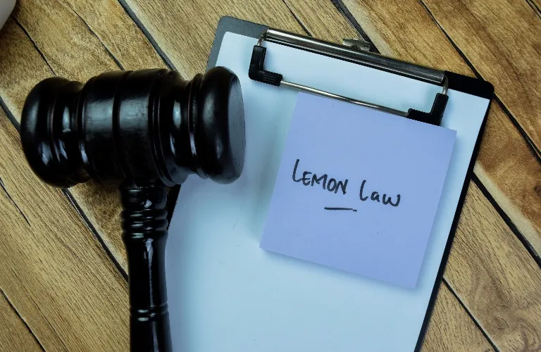 Wooden judge's gavel beside clipboard with a note labeled "Lemon Law" on wooden surface.
