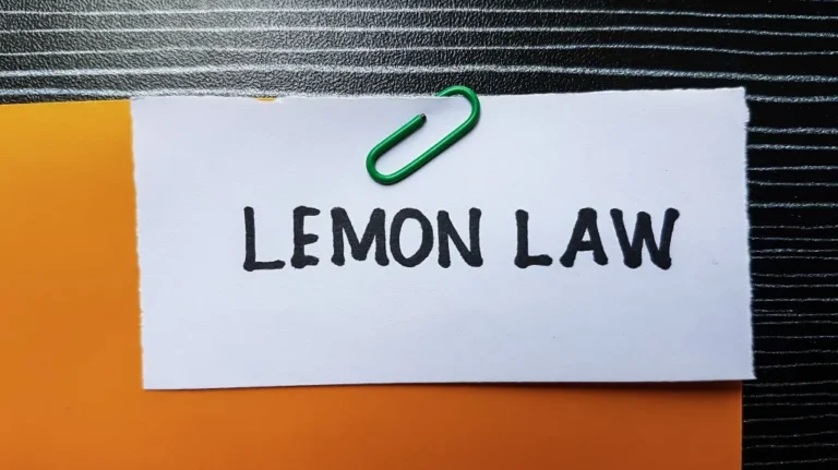White paper with "LEMON LAW" text clipped by green paperclip on orange and black textured surface.