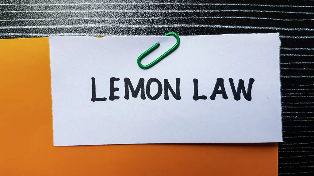 White paper with "LEMON LAW" text clipped by green paperclip on orange and black textured surface.