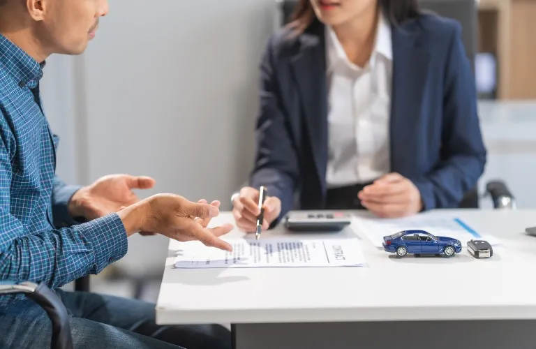 Two professionals discussing a contract at a white desk with a blue toy car and car keys.