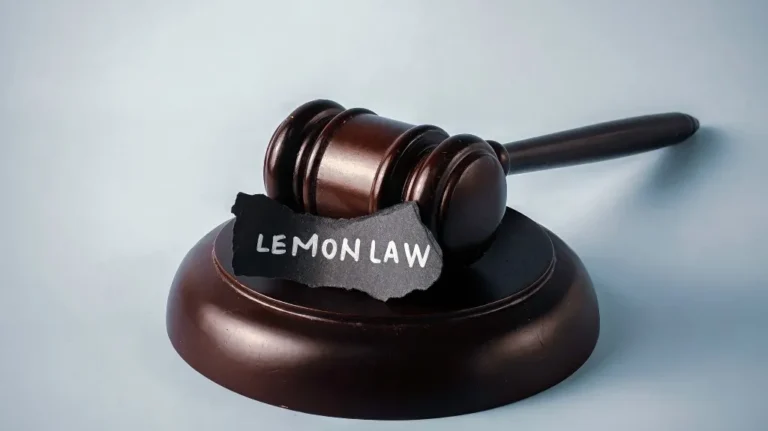 Wooden judge's gavel resting on sound block with torn paper labeled "LEMON LAW