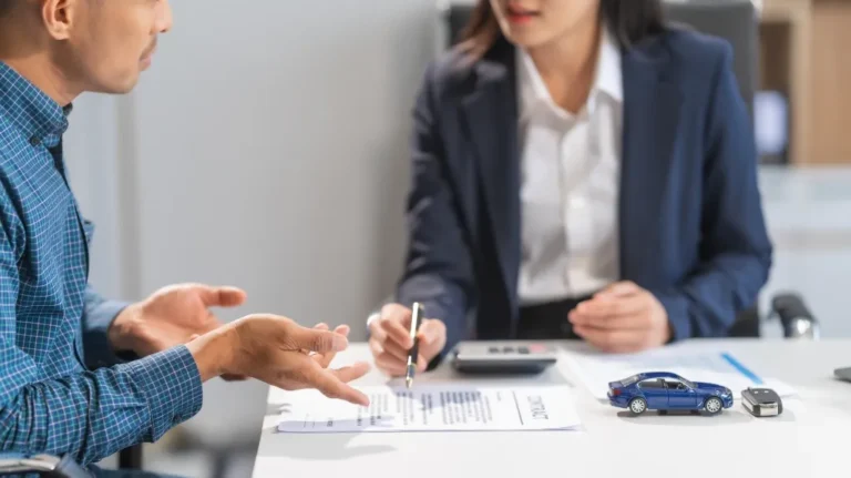 Two professionals discussing a contract at a desk with blue toy car and remote key.
