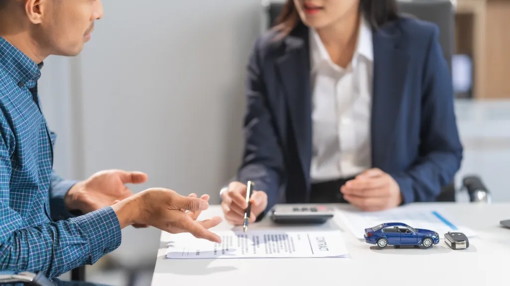 Two professionals discussing a contract at a desk with blue toy car and remote key.