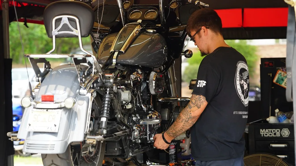 Man with tattoos working on a black motorcycle in a garage with Matco Tools visible.
