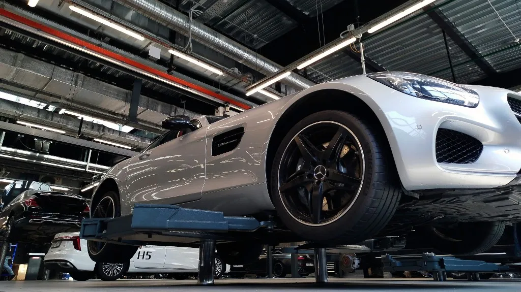 White Mercedes-Benz sports car elevated on a hydraulic lift inside a modern automotive workshop.
