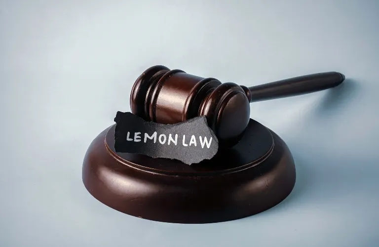 Dark wooden judge's gavel resting on a sound block with "LEMON LAW" text on torn black paper.