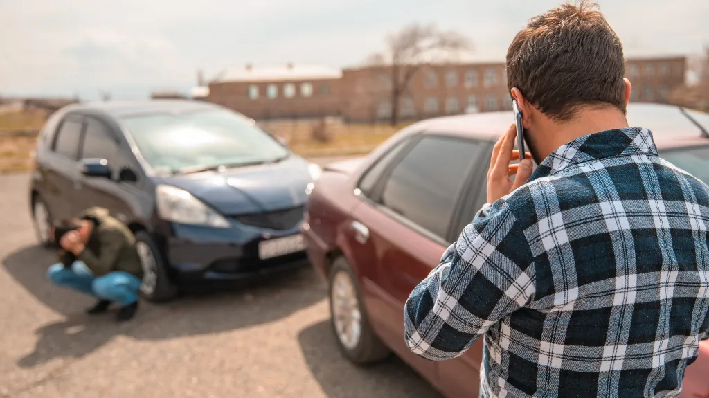 Two men near a black and maroon car after a minor accident, one on phone.