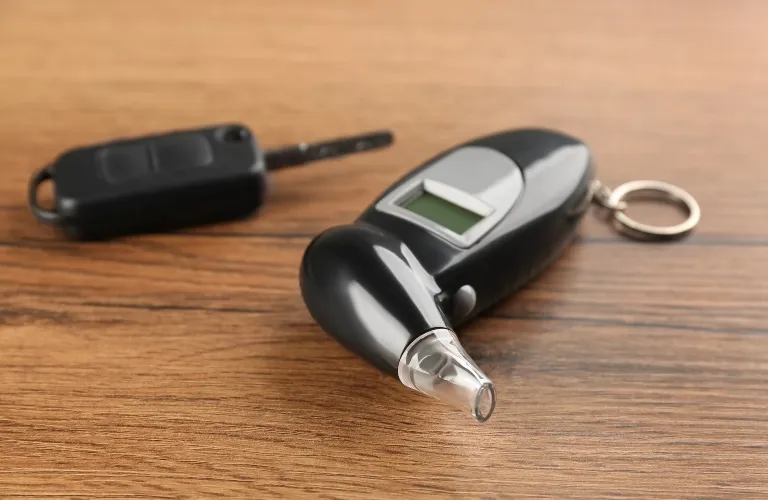 Black digital breathalyzer device with keychain and car key on wooden surface.
