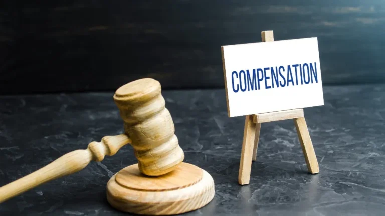Wooden judge's gavel beside a small easel with a card reading "COMPENSATION" on a dark surface.